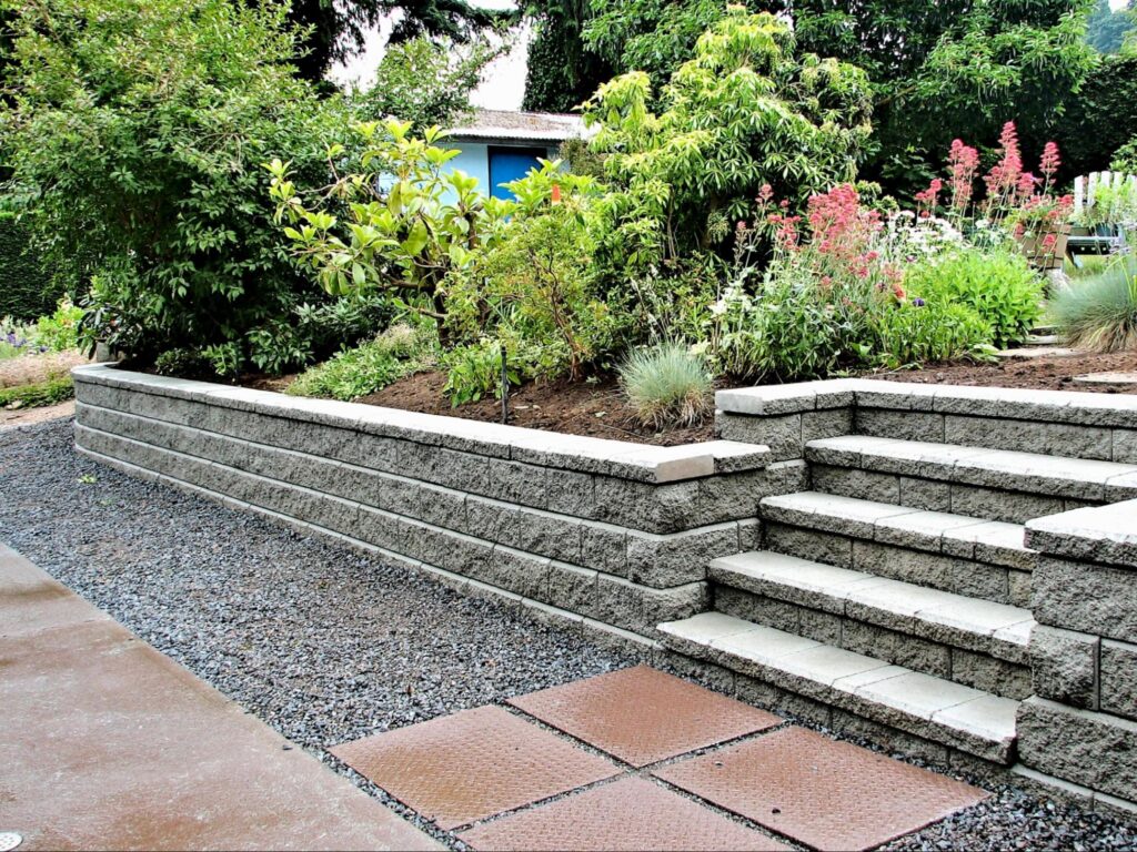 Landscape design in Hingham, MA with a stone retaining wall, steps, and raised planting bed.