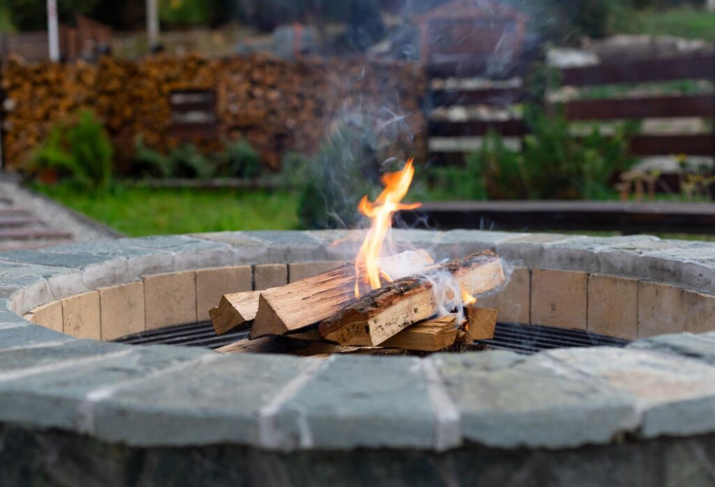 Stone fire pit design burning wood in a landscaped backyard setting. 