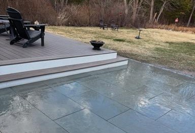 A bluestone outdoor patio with steps up to a deck at a Hingham, MA home.
